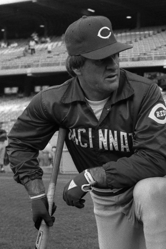 Pete Rose, Cincinnati Reds player-manager, kneeling with a bat in a Reds cap and Cincinnati warm-up jacket before a game at Dodger Stadium, 1985