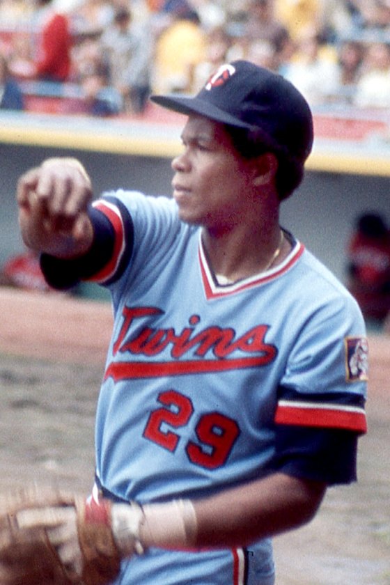 Rod Carew in a navy Twins cap and powder-blue Minnesota Twins road uniform with No. 29, warming up before a game at Cleveland Stadium, 1975